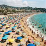 Crowded Mediterranean beach with colorful umbrellas, swimmers, boats, and hot air balloon